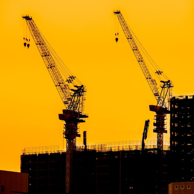 Foto lage hoek van silhouetkranen op de bouwplaats tegen de hemel tijdens zonsondergang