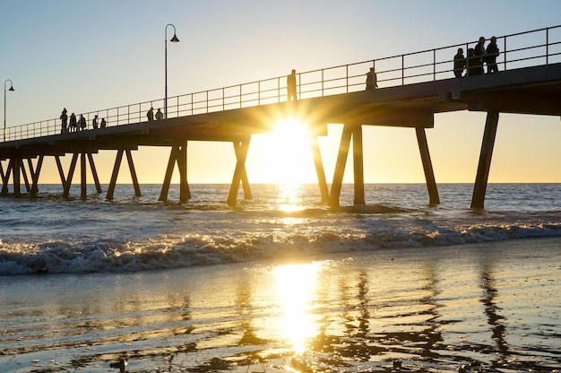 Lage hoek van silhouetten van mensen die tijdens de zonsondergang op de pier over zee op het strand van glenelg lopen