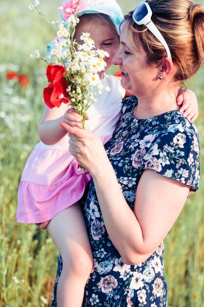 Foto lage hoek van vrouw die dochter draagt en een boeket bloemen vasthoudt