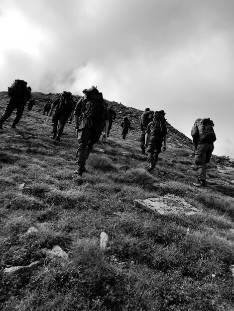 Foto lage hoek van wandelaars met rugzakken die op de berg klimmen tegen de lucht