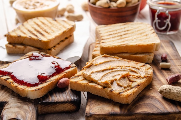 Lage hoekmening op boterhammen met pindakaas en jam op snijplank met toast opzij. Gezond eetconcept