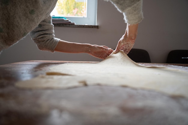 Lage hoekmening van een vrouw die een zelfgemaakt filodeeg-strudeldeeg rolt en trekt op een eettafel thuis