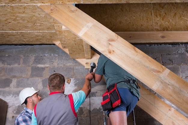 Lage hoekmening van team van bouwvakkers die houten trapframe bouwen in onvoltooide nieuwe woning