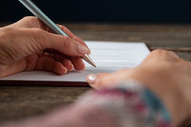 Lage hoekmening van vrouwelijke hand ondertekening van een document, aanvraagformulier of contract met een pen op rustieke houten bureau.