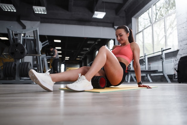 Lage hoekopname van een vrouwelijke atleet die ontspant na een beentraining, met schuimroller op de hamstrings