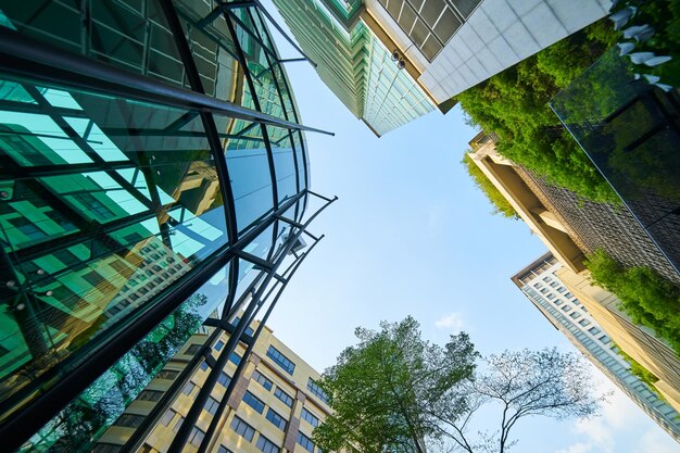 Lage hoekopname van moderne glazen gebouwen en groen met heldere hemelachtergrond.