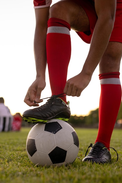 Lage sectie van blanke mannelijke atleet die rode sokken draagt met been op voetbal die schoenveter koppelt