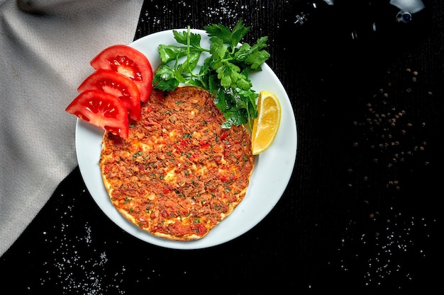 Lahmacun is a popular turkish dish. thin crispy tortilla with minced lamb, tomatoes and bell pepper on black table