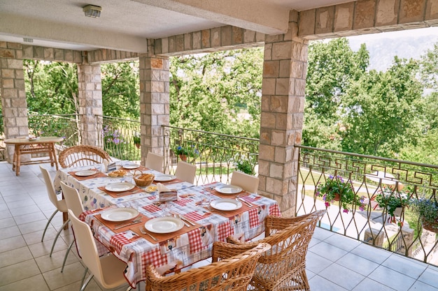 Laid festive table surrounded by rattan chairs stands on the terrace of a stone villa in a green