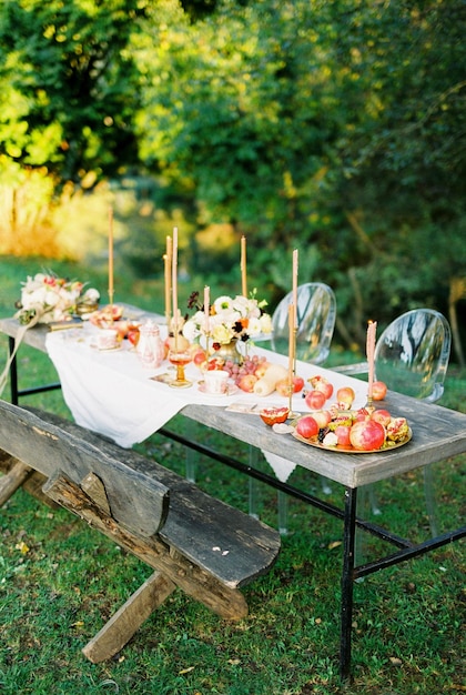 Laid table with fruits and candles in the garden near a bench and chairs