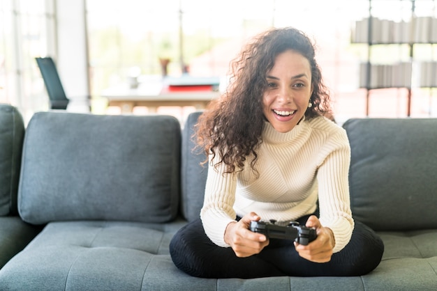 Foto donna latina che gioca ai videogiochi con le mani che tengono il joystick sul divano di casa