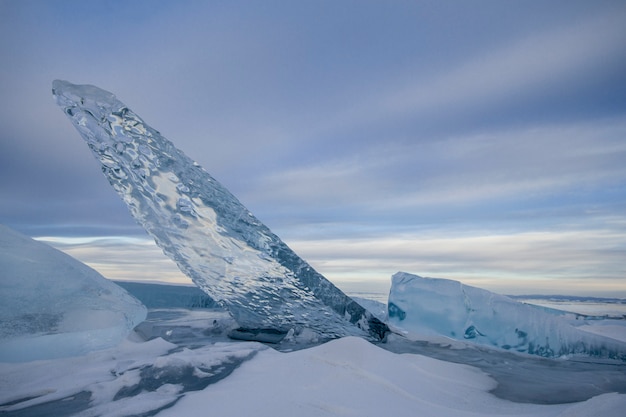 Lake Baikal is covered with ice and snow, strong cold, thick clear blue ice. Icicles hang from the rocks