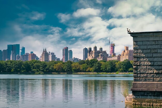 Photo lake in park with city skyline against blue sky and clouds