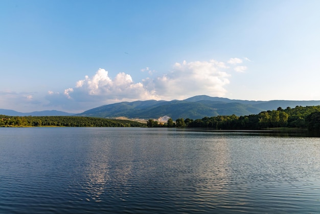 A lake reflects sunlight against blue sky and mountain ranges and villages