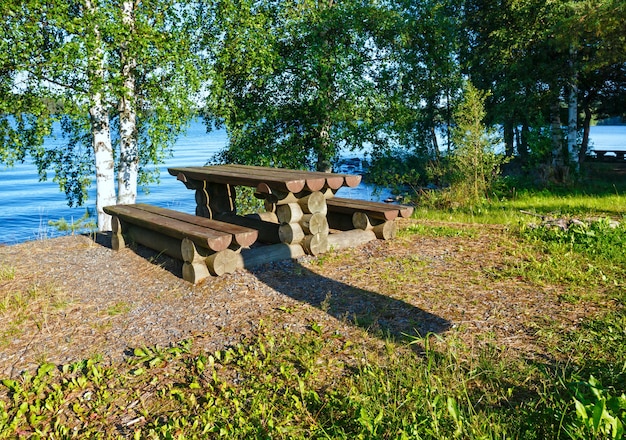 木々と端に木製のテーブルがある湖の夏の景色（フィンランド）。