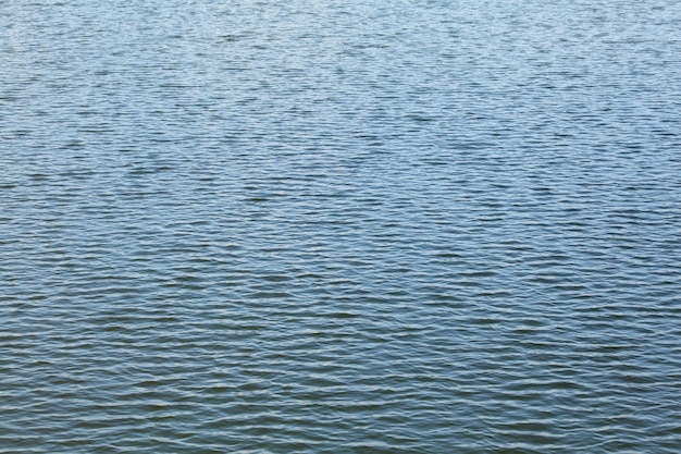 Поверхность озера, вода почти спокойная, лишь небольшие волны. Абстрактный водянистый фон.