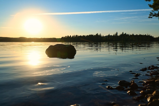 Озеро в Швеции маленькое и на закате со скалой на переднем плане воды с лесом