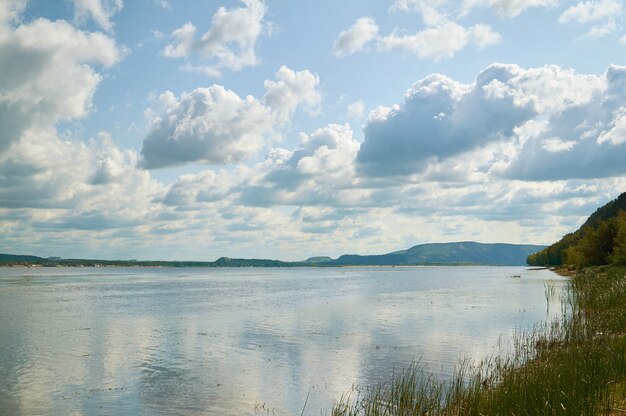 Lake with grassy shore and clouds in the blue sky.                               