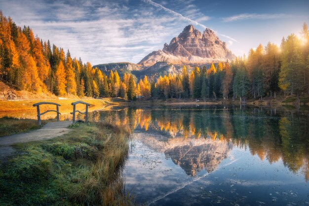 Photo lake with reflection in mountains at sunrise in autumn in dolomites italy landscape with antorno lake small wooden bridge trees with orange leaves high rocks blue sky in fall colorful forest