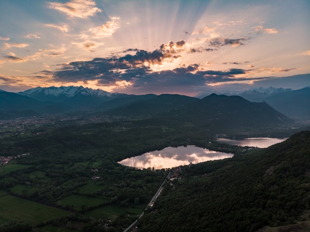 Lakes at sunset, reflection of snowcapped mountain range and scenic colorful sky, sun rays beyond the clouds.