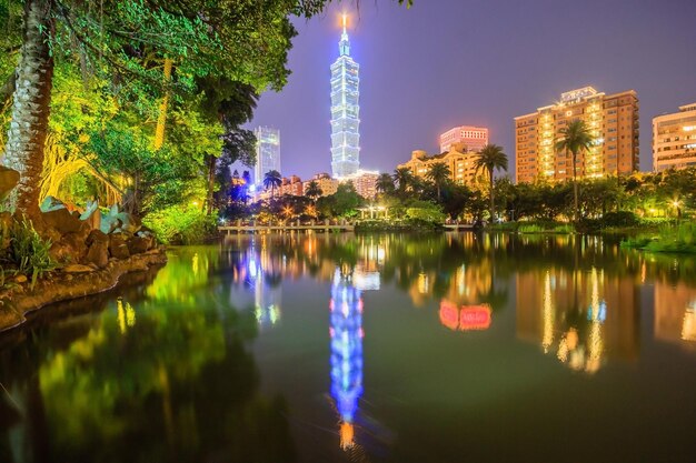 Lakeside scenery of Taipei 101 Tower among skyscrapers in Xinyi District Downtown at night with view of reflections on the pond in an urban park Romantic nightscape of Taipei city