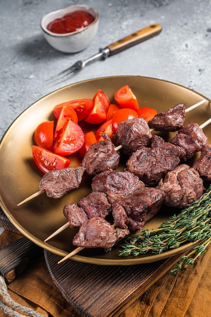 Lam shish kebab gegrilde spiesjes in een bord met tomaat. Grijze achtergrond. Bovenaanzicht.