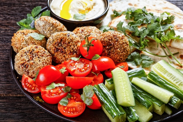 Lamb meatballs served with flatbread, fresh cucumber, tomatoes and hummus on a black plate on a wooden table