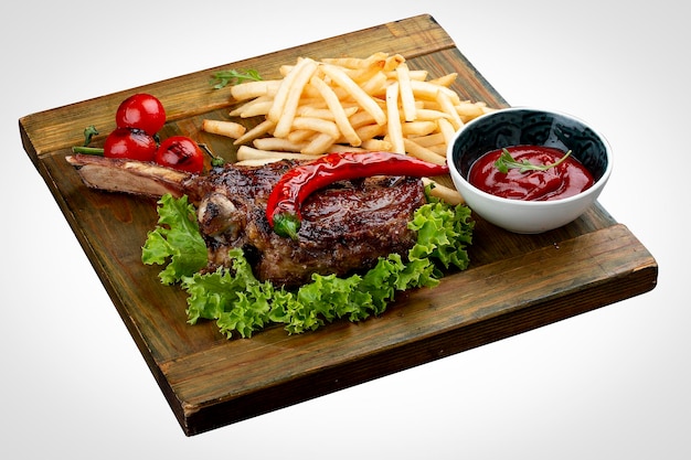 Lamb rack with fries and sauce on a wooden board on a white\
background