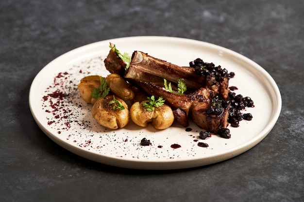 Lamb ribs with baked potatoes on a white plate, close-up.