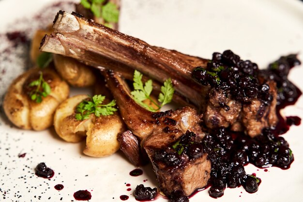 Lamb ribs with baked potatoes on a white plate, close-up.