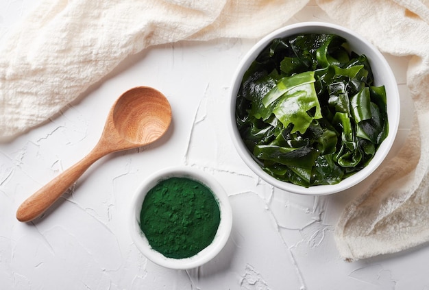 laminaria kelp seaweed and spirulina powder in white bowl background