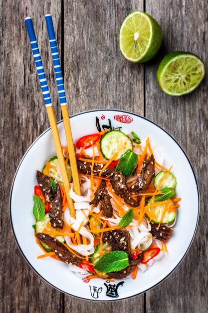 Lamsnoedelsalade met komkommer, wortelen, chilipepers en munt op houten tafel