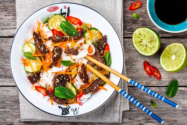 Lamsnoedelsalade met komkommer, wortelen, chilipepers en munt op houten tafel