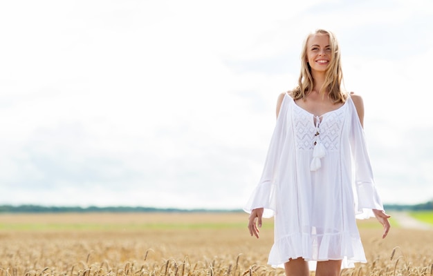 Foto land, natuur, zomervakantie, vakantie en mensen concept - lachende jonge vrouw in witte jurk op graanveld