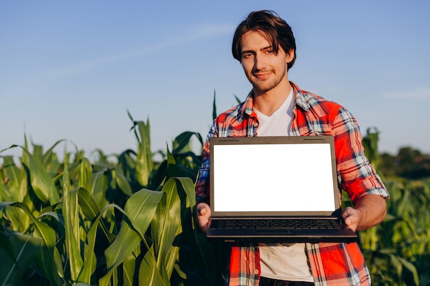 Landbouwer die zich op een gebied bevindt dat open laptop houdt. Wit scherm mockup