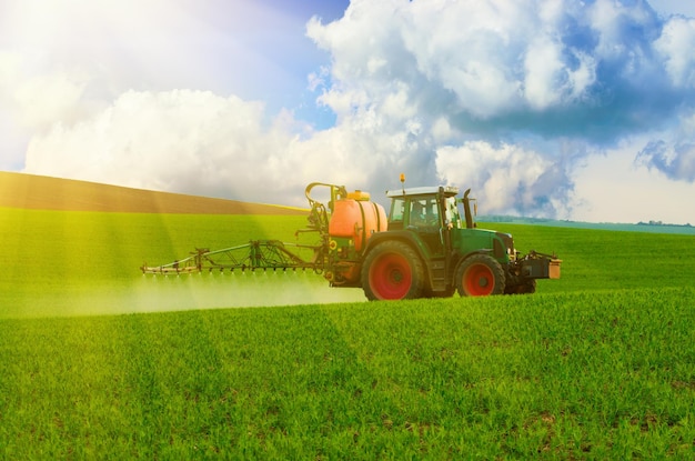 Landbouwmachines die insecticide naar het groene veld spuiten, agrarische natuurlijke seizoensgebonden lente-achtergrond