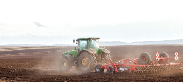 Landbouwtractor land voorbereiden met zaaibedcultivator als onderdeel van pre-zaaiactiviteiten in het vroege voorjaar van landbouwwerkzaamheden op landerijen