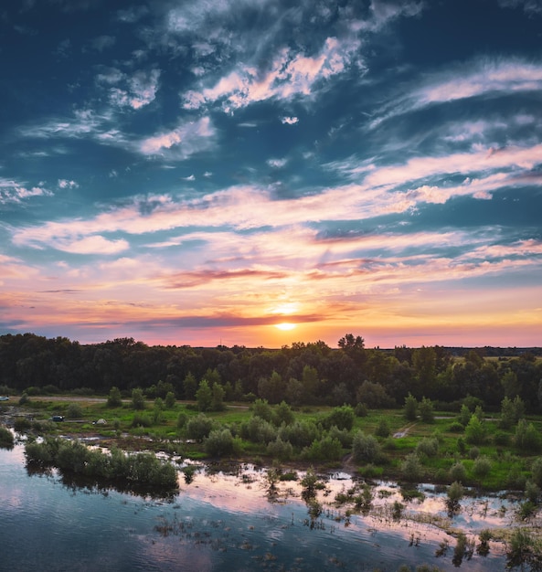 Landelijk zomerzonsonderganglandschap met rivier en dramatische kleurrijke lucht natuurlijke luchtfoto als achtergrond