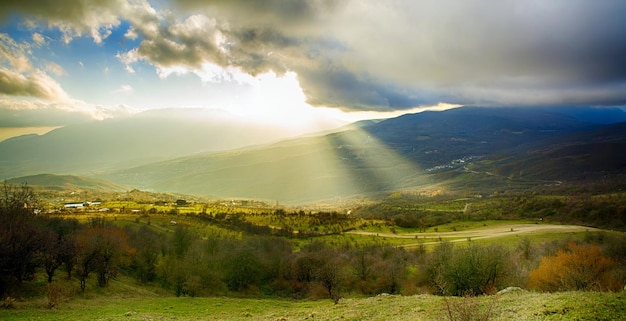 Landelijk zonsonderganglandschap met groene heuvels, dramatische lucht, bergen en zonnestralen