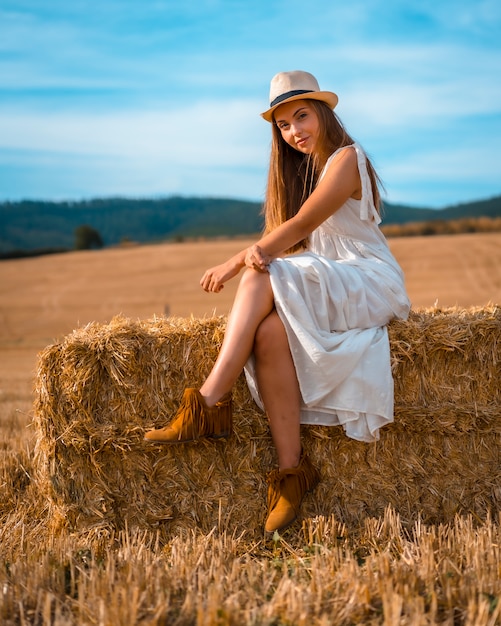 Landelijke levensstijl, portret van een jonge blanke blonde boer in witte jurk en een hoed