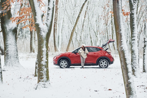 Landelijke scène Mooie jonge vrouw is buiten in de buurt van haar rode auto in de winter