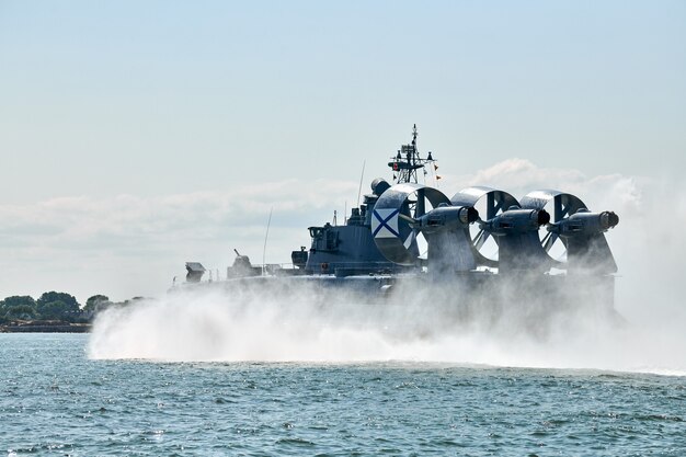 Photo landing craft air cushion lcac hovercraft landing craft sailing splashing sea water at high speed. hover craft flying above water, air cushion sailing near port at baltic sea. russian navy