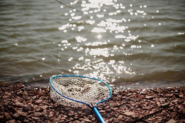 Premium Photo  Landing net lies on the rocky shore of the lake in sunny  weather. silicone landing net on the lake