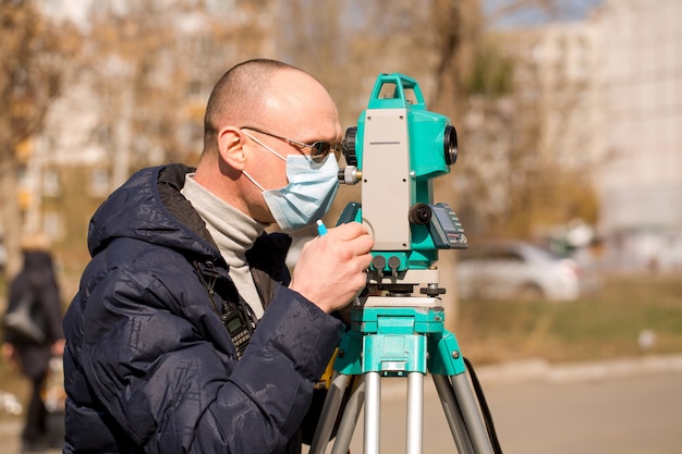 Landmeter met beschermend masker werkt met een total station