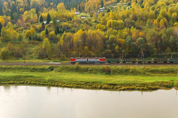 Landscape autumn river valley with a village between wooded hills and the railroad along which the freight train goes