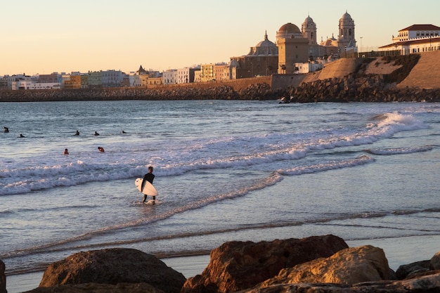 スペインの夕暮れ時にサーファーでいっぱいのビーチのあるカディス湾の風景