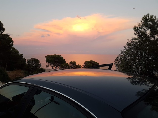Landscape of a beach in the distance during sunset with the sky reflected in a car