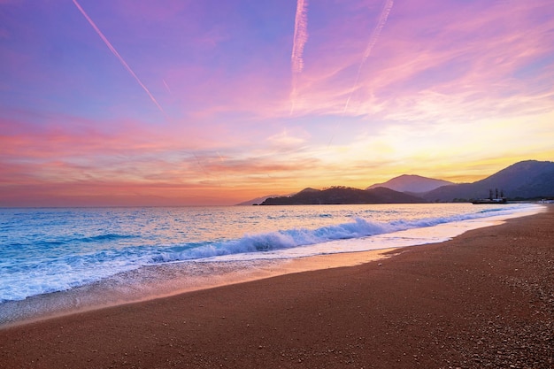 牧歌的な夕焼けのグラデーションの空と白い泡が立ち込める青い海の浜辺の風景