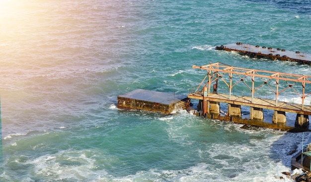 A landscape of blue sea and sky with an old sea pier on a cliff background on a bright sunny day.