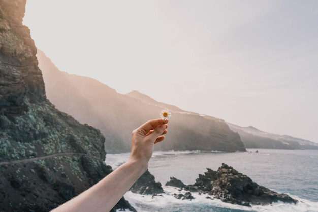 Photo landscape in the foreground holding a daisy with a volcanic beach in the background at sunset